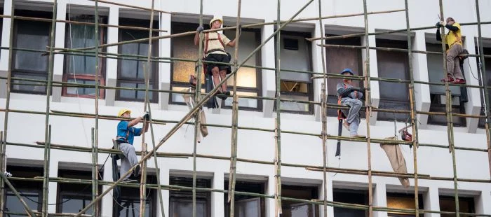 Stavební dělníci pracují na lešení u budovy.
