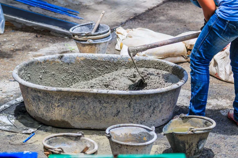 Pracovník míchá beton v plastovém kbelíku na staveništi.