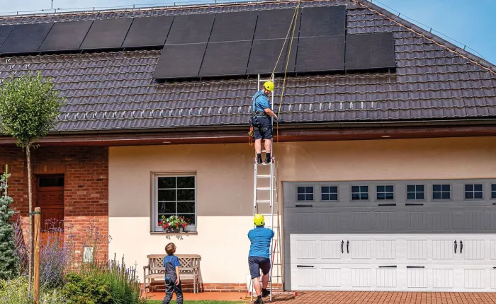 Dva dělníci montují fotovoltaické panely na střechu rodinného domu.
