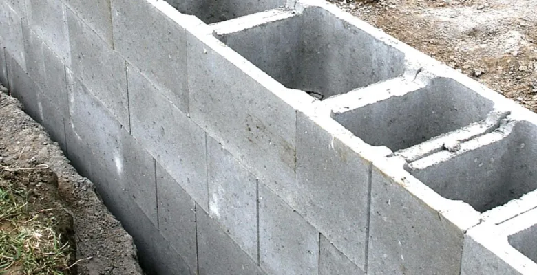Stavba zdi ze železobetonových bloků na výkopu.