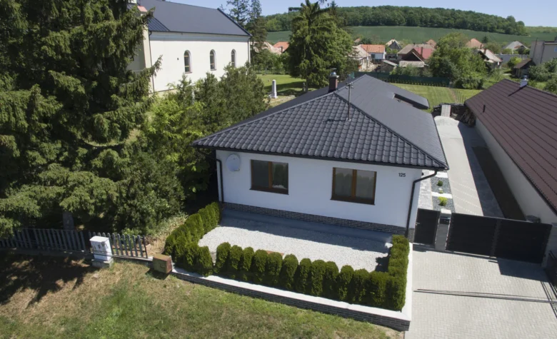 Moderní dům s dvousklonovou střechou pokrytou tmavými taškami.