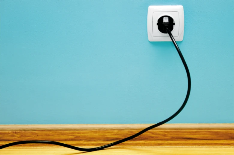 Černá elektrická zástrčka v bílé zásuvce na modré stěně.