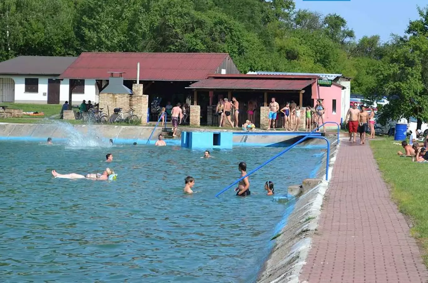 Venkovní bazén ve Všejanech s plavci a přístřeškem pro šatny.