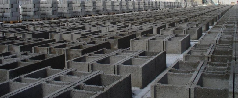 Řady betonových dutých bloků v bednění na výrobním podlaze.
