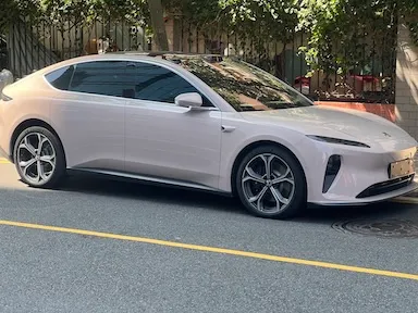 Bílé elektromobil zaparkovaný na ulici vedle stromů.