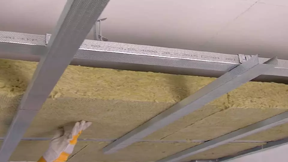Montáž žluté izolační vaty mezi ocelové nosníky stropu nebo zdi.