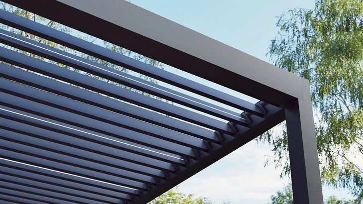 Moderní tmavá bioklimatická pergola s lamelami na pozadí stromů.