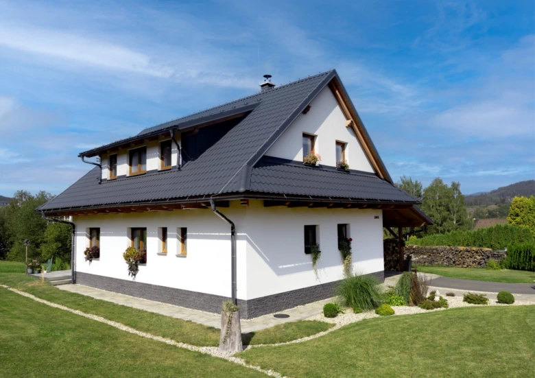 Moderní dům s tmavou hliníkovou střešní krytinou na pozadí modré oblohy.