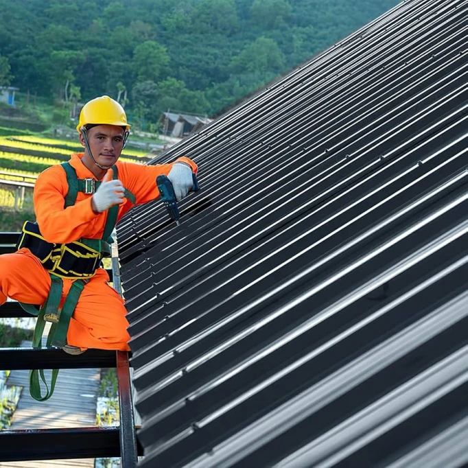 Montáž trapézových plechů na střechu pracovníkem s elektrickým nářadím.