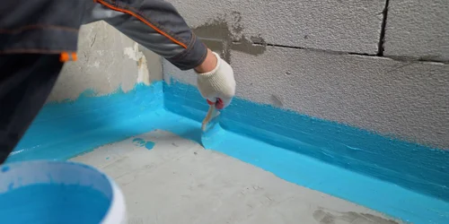 Práce na hydroizolaci koupelny nanášením modré barvy.