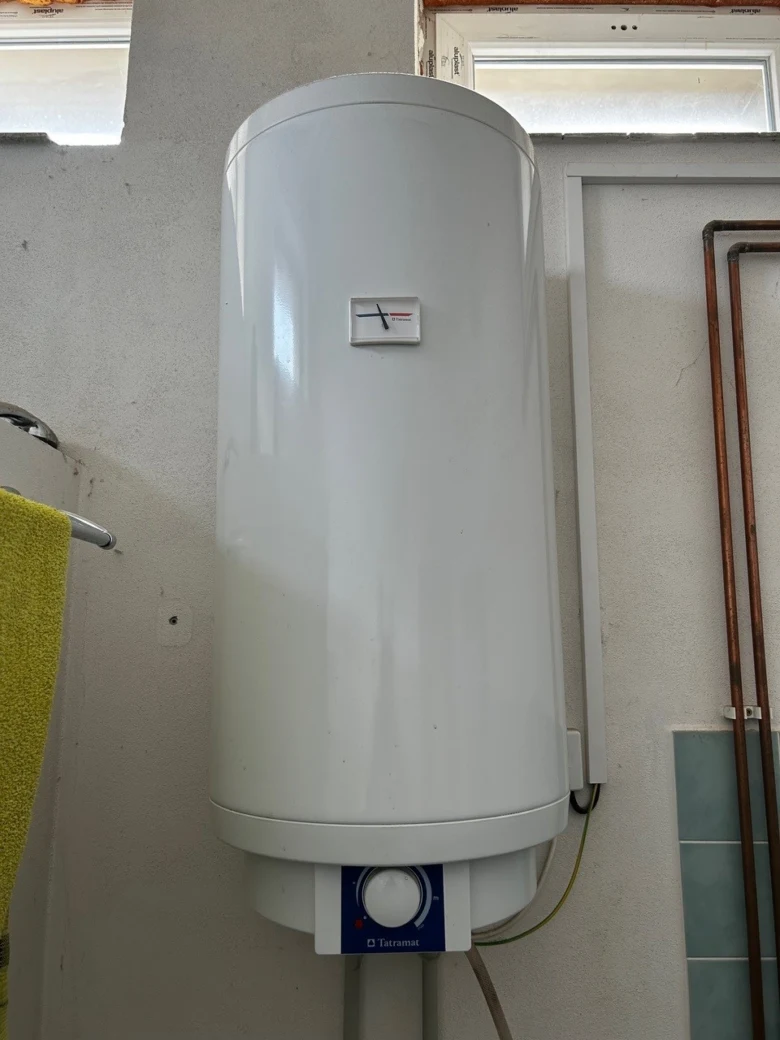 Bílý elektrický bojler na zdi s měřidlem teploty a ovládacím panelem.