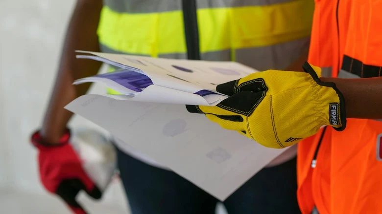 Stavební dělníci s dokumentací v rukou na staveništi.