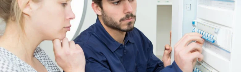 Elektrikář upravuje jističe v rozvaděči před ženou.