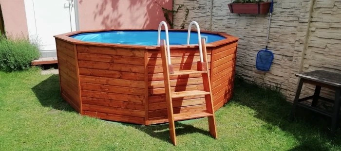 Nadzemní bazén s dřevěným obložením a schodištěm na trávníku.