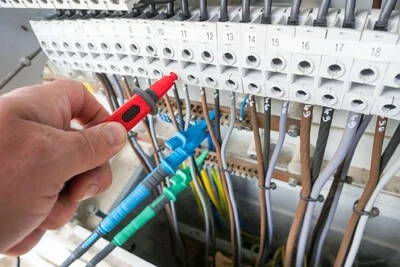 Ruční kontrola elektrického rozvaděče pomocí měřicího přístroje.