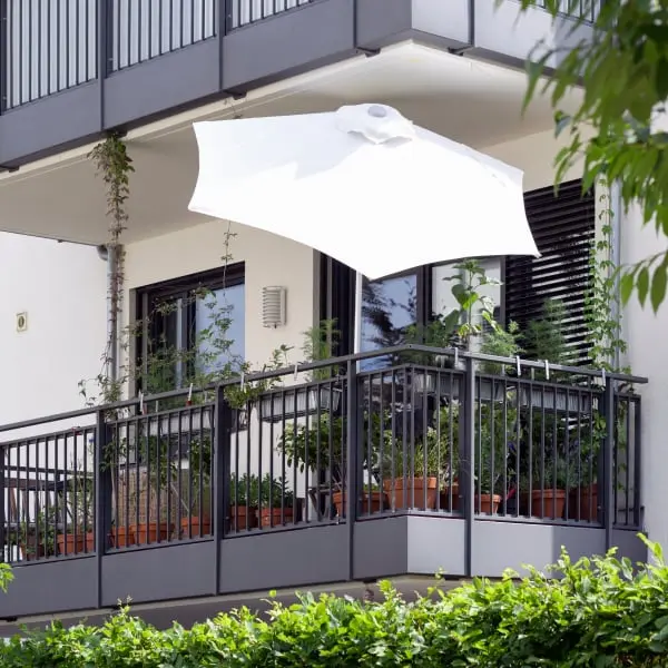 Balkon v panelovém domě zastíněn bílou parasolkou s rostlinami.