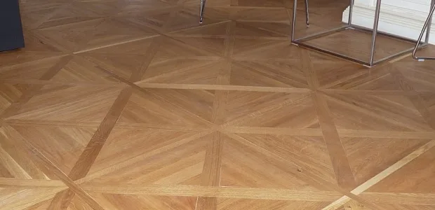 Pohled na lakovanou parketovou podlahu s geometrickým vzorem.
