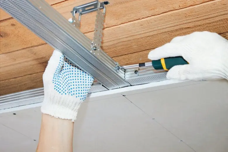 Ruční montáž kovových profilů pro sádrokarton na dřevěné trámy.