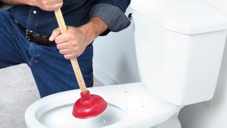 Muž používá hadicovou pumpu na uvolnění ucpaného záchodu.