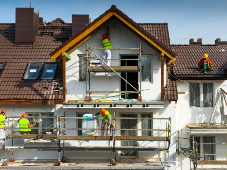 Pracovníci zateplují fasádu domu minerální vlnou na provizorním schodišti.