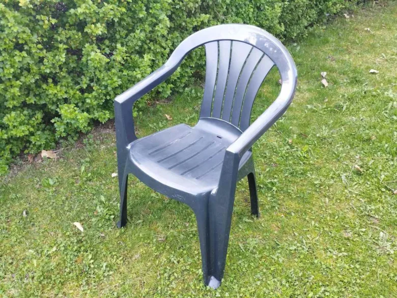 Šedé plastové zahradní křeslo na trávě u keře.
