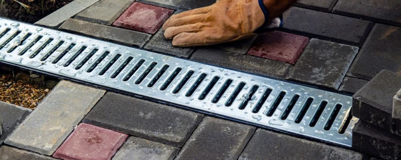 Instalace kovového odvodňovacího žlabu mezi dlažebními kostkami.