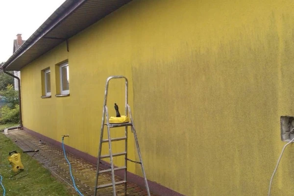 Žlutá fasáda domu s špinavými stopy při čištění pomocí žebříku.