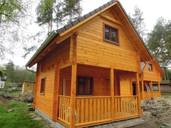 Nově postavená dřevěná chata s podkrovím a menšími stavbami v lese.