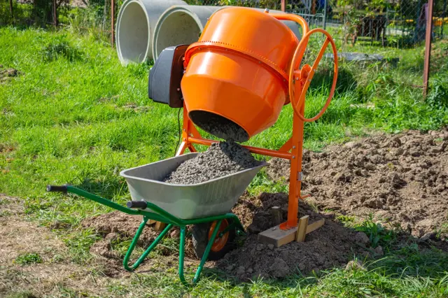 Oranžový betonová směšovač nalévá čerstvý beton do vozíku.