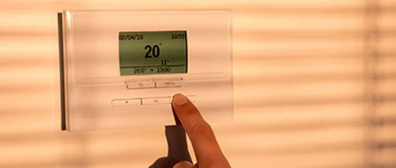 Ruka nastavuje teplotu na digitálním termostatu pro úsporu energie.