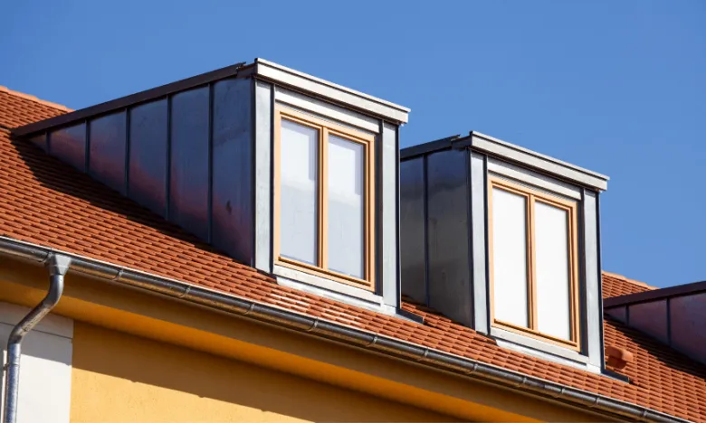 Detailní pohled na konstrukci vikýřů s okny na červené střechě domu.