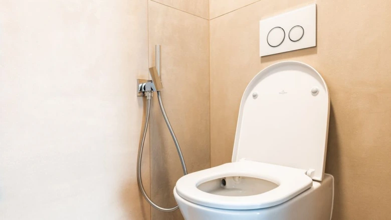 Moderní záchod s připojenou stěnovou mycí hadicí pro hygienu.
