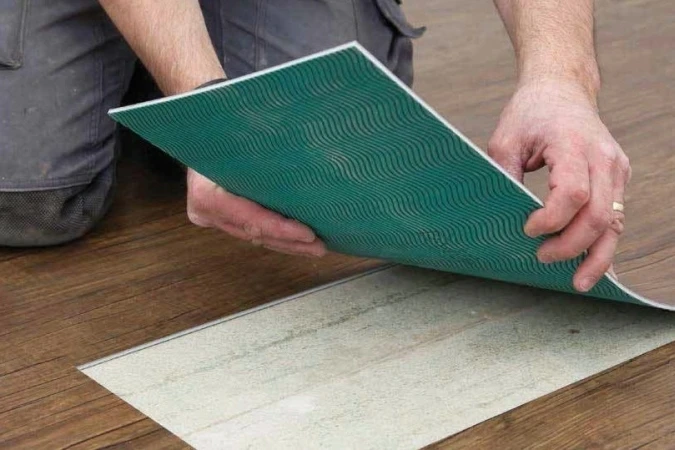 Muž pokládá vinylovou podlahu s lepidlem na zadní straně.