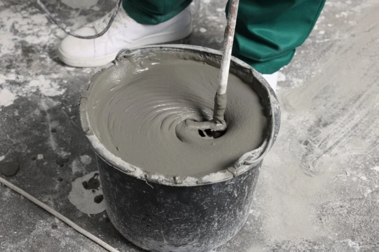 Pracovník míchá beton v kbelíku na podlahu.
