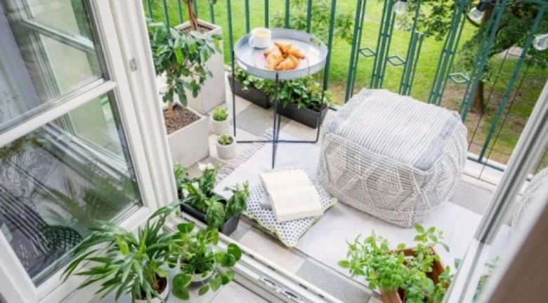 Zelený balkon s rostlinami, sedací křeslem a knihou.