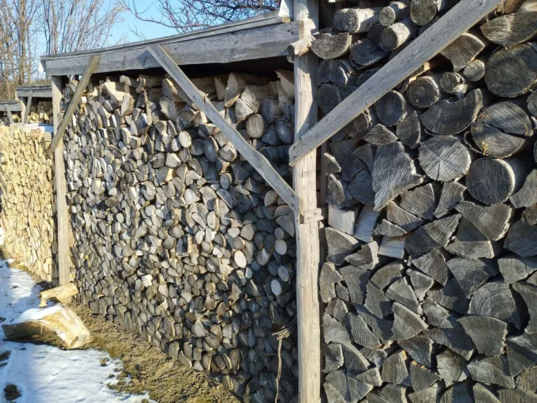 Dřevník s přístřeškem plný naloženého dříví venku.