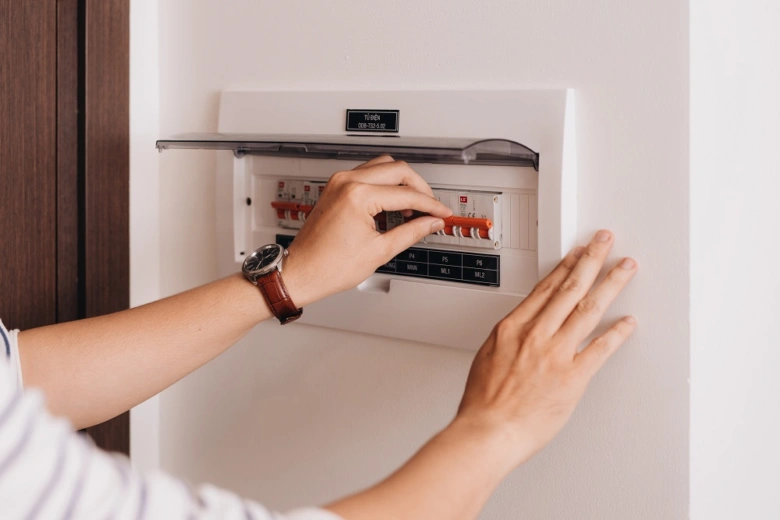Ruka resetuje jistič v elektrickém rozvaděči na zdi.