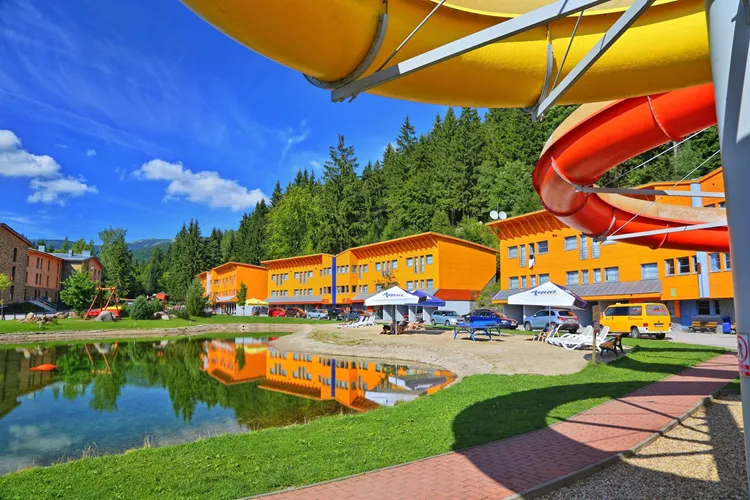 Venkovní aquapark s barevnými skluzavkami a oranžovými budovami v Špindlerově Mlýně.