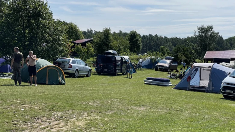 Kempování v kempu Milavy s stanu, auty a lidmi na trávníku.