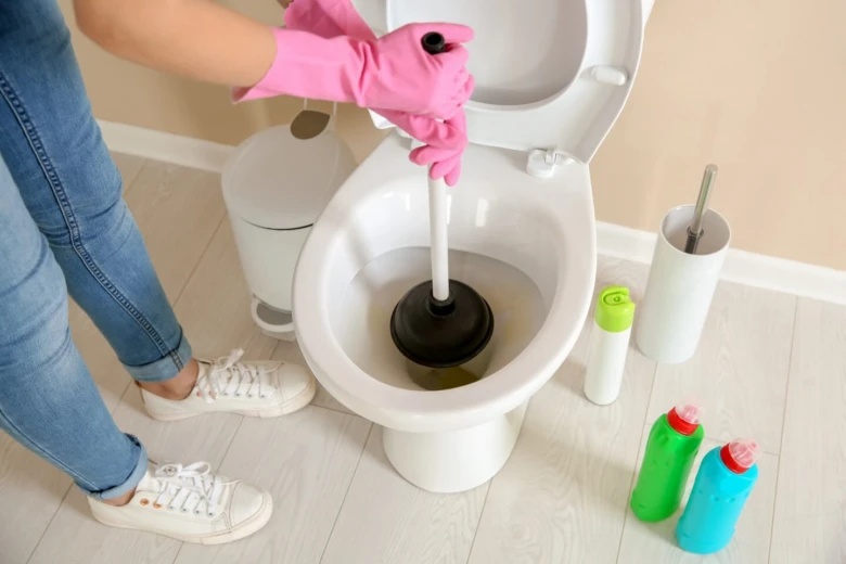 Osoba s růžovými rukavicemi uvolňuje ucpaný záchod pomocí hadice.
