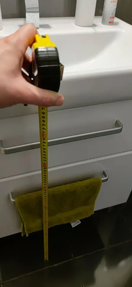 Ruční měření výšky umyvadla v koupelně páskou.