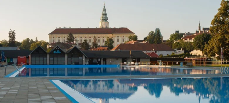 Venkovní plavecký bazén s historickým zámekem na pozadí.