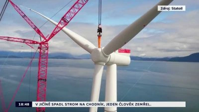 Červený kran zvedá bledou lopatku větrného turbínu.