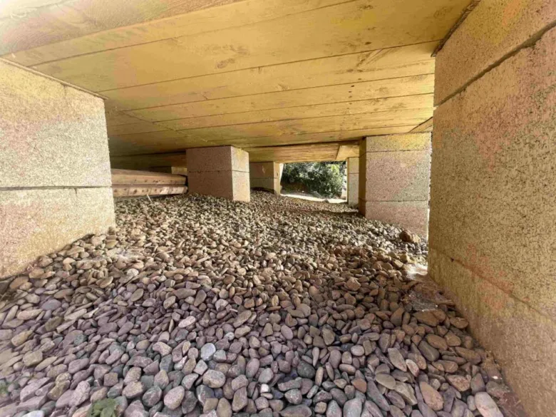 Konkrétní betonové patky pod dřevěnou stavbou s kamenivem.