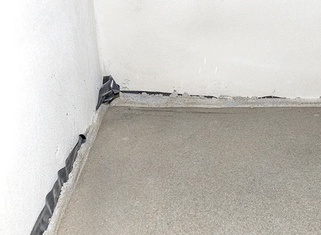Detail dilatační spáry podlahy s černou páskou v rohu.