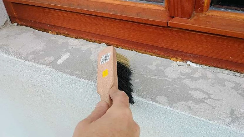 Ruka čistí betonový parapet pod dřevěným oknem před montáží.
