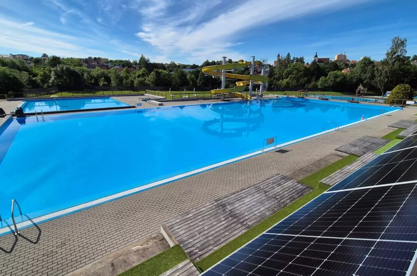 Venkovní bazén ve Vlašimi s vodními skluzavkami a solárními panely.