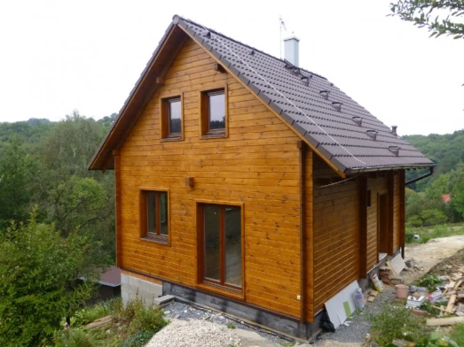 Dřevěná chata s podkrovím na kopci v přírodě.