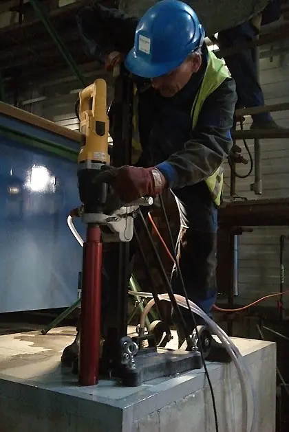 Pracovník provádí jádrové vrtání do betonu pomocí speciálního stroje.