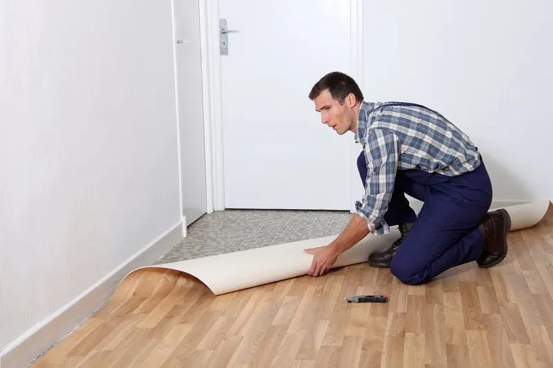 Muž pokládá linoleum na podlahu v interiéru.